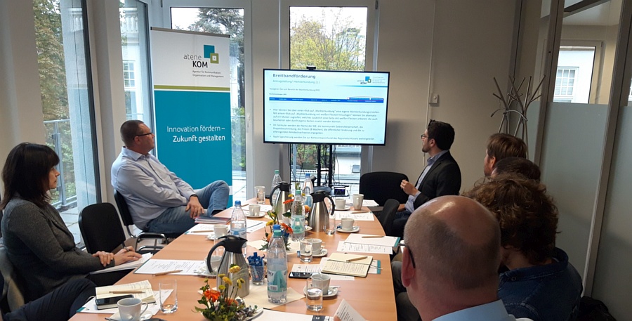 Udo Kirsch (vor dem Monitor links) und Hardy Stecker (vor dem Monitor rechts) mit Teilnehmern beim Workshop zur Bundesförderung Breitband im Regionalbüro für Nordrhein-Westfalen der aconium GmbH (Projektträger für das Bundesförderprogramm Breitband des BMVI). Bonn, 02. Oktober 2018.